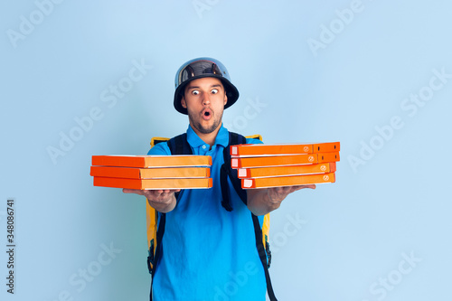 Proposing pizza. Emotions of caucasian deliveryman isolated on blue background. Contacless delivery service during quarantine. Man delivers food during isolation. Safety. Hurrying up. Looks fun. photo