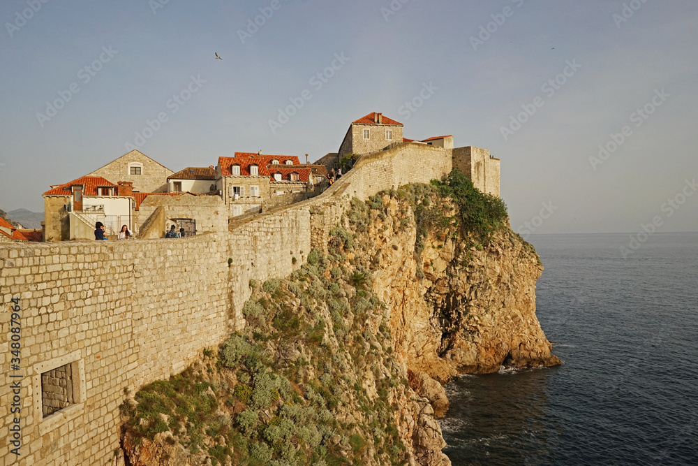 Exterior architecture and design of Dubrovnik old town city walls and landscape with clear blue sky, southern Croatia fronting the Adriatic sea encircled with massive stone Exterior architecture and design of Dubrovnik old town city walls and landscape with clear blue sky, southern Croatia fronting the Adriatic sea encircled with massive stone