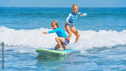 Canvas Print Happy baby boy and girl - young surfers ride with fun on one surfboard