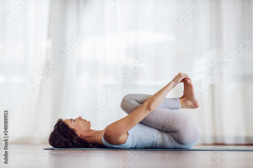 Side view of fit slim yogi girl in Happy Baby yoga pose. Yoga studio interior.
