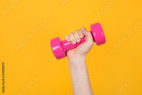 Working out concept. Cropped photo of a sportive woman holding pink dumbbell in her hand isolated on yellow background photo