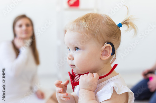 Hearing aid in baby girl's ear. Toddler child wearing a hearing aid at home. Disabled child, disability and deafness concept. photo