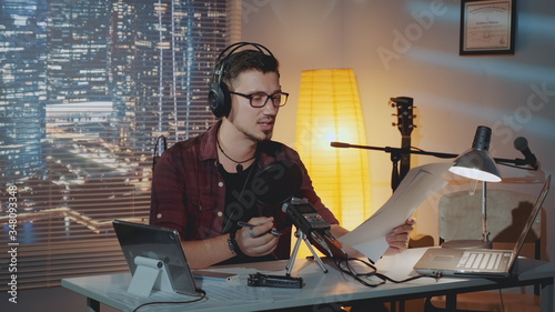 Home recording studio: the speaker in headphone reads the story into the microphone. There is a computer and other recording equipment on the table.