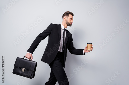 Profile side photo of serious worker man late work rest relax time hurry workplace hold espresso beverage mug briefcase wear black pants jacket blazer isolated grey color background photo