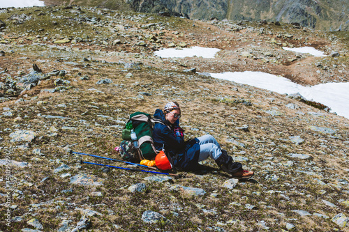 Young girl tourist mountaineer in special clothes and backpack sitting on a mountain surface and resting after conquering the summit. Concept of outdoor activities.