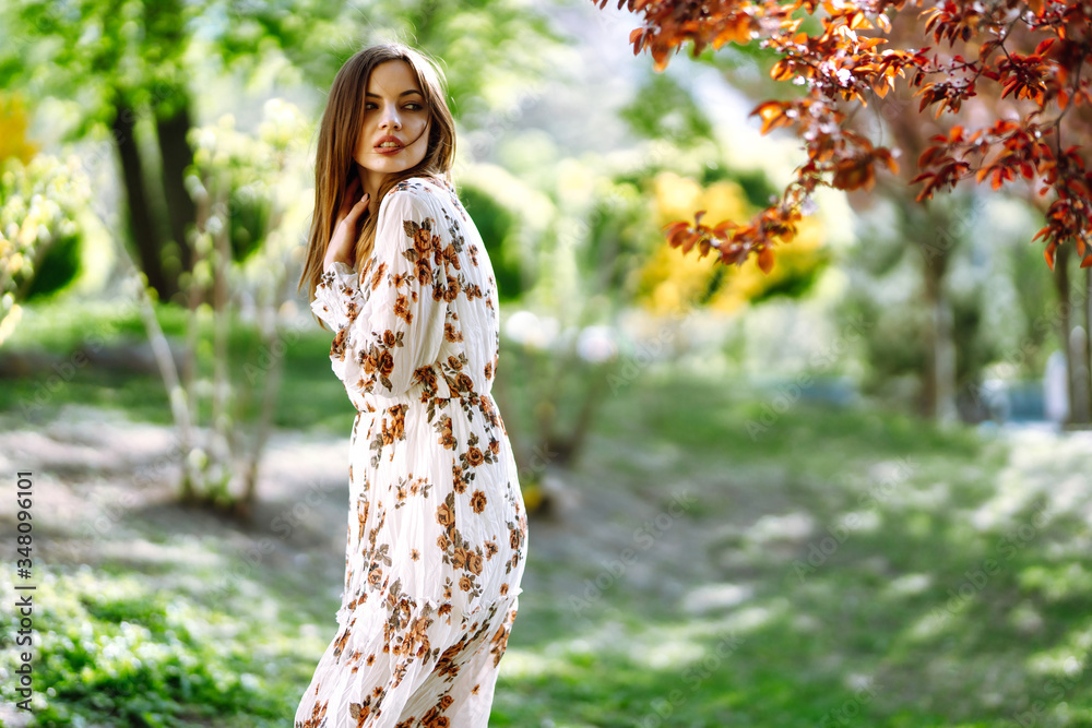 Portrait of attractive woman in a pretty dress with flowers enjoys blooming green garden in spring day. Fashion and style concept. Portrait of attractive woman in a pretty dress with flowers enjoys blooming green garden in spring day. Fashion and style concept.