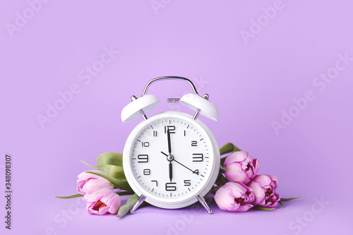 Alarm clock and flowers on color background. Spring time photo