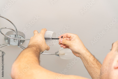 a man’s hand twists a light bulb from a lampshade. bulb replacement, lamp twist. photo