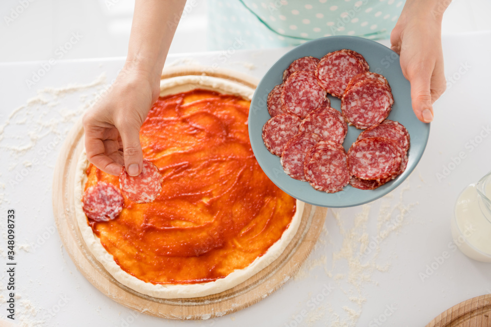 Cropped photo of housewife hands cooking family recipe dinner covering dough pizza ingredients fresh slices sausage standing modern kitchen indoors Cropped photo of housewife hands cooking family recipe dinner covering dough pizza ingredients fresh slices sausage standing modern kitchen indoors