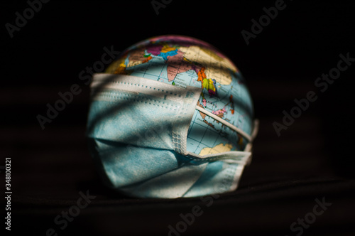 Earth globe with geografical names in Ukrainian cyrillic letters on it dressed in a surgical mask on black background. Coronavirus epidemic in world, pandemic danger, global quarantine concept photo