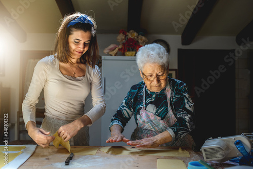 Portrait of caucasian grandmother and granddaughter smiling preparing dough for making fresh homemade pasta. Spending time together in family. Traditional Italian food. 