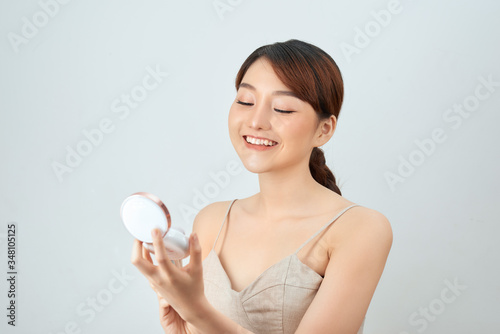 Portrait of a young beautiful woman applying foundation over white background