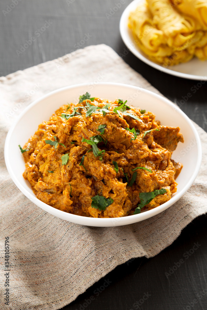 Homemade Chicken Tikka Masala in a white bowl on a black surface, side view. Homemade Chicken Tikka Masala in a white bowl on a black surface, side view.
