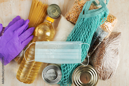 food donations, medical mask and gloves with a blue string bag on a light wooden background