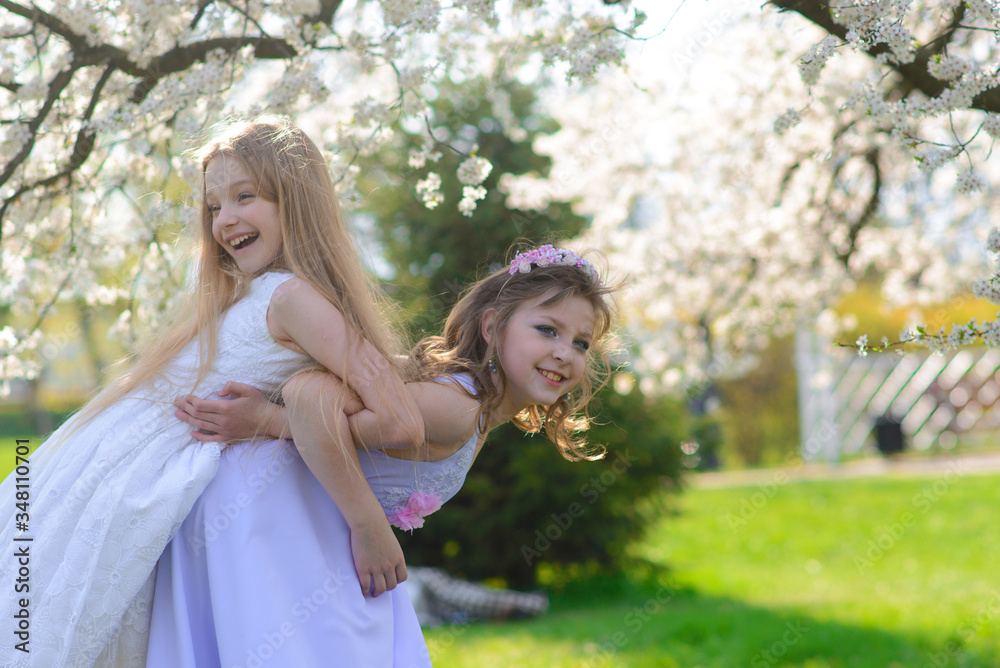 Beautiful young girls with blue eyes in a white dresses in the garden with apple trees blosoming having fun and enjoying smell of flowering spring garden. Beautiful young girls with blue eyes in a white dresses in the garden with apple trees blosoming having fun and enjoying smell of flowering spring garden.