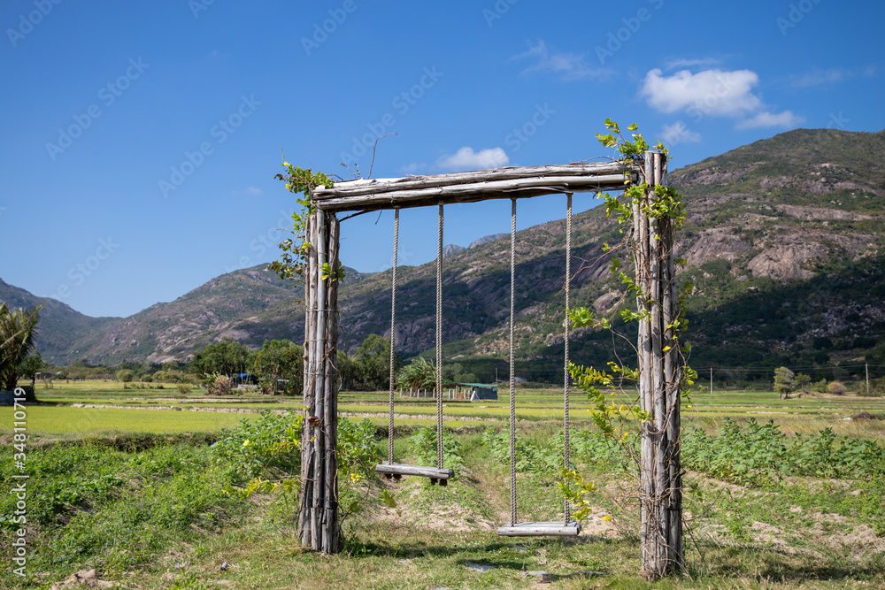 Wooden swing covered with green climbers on the background of the mountains