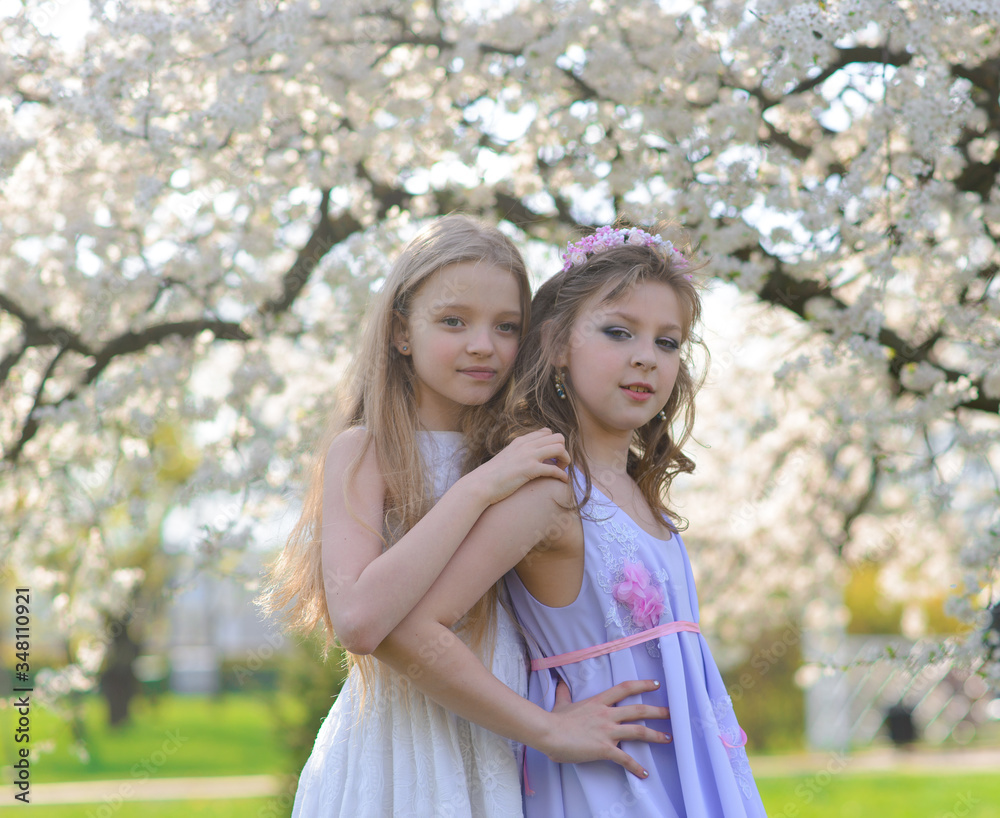 Beautiful young girls with blue eyes in a white dresses in the garden with apple trees blosoming having fun and enjoying smell of flowering spring garden. Beautiful young girls with blue eyes in a white dresses in the garden with apple trees blosoming having fun and enjoying smell of flowering spring garden.