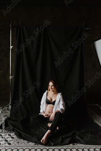 Beautiful pregnant woman in underwear and a shirt in the studio on a fabric background.