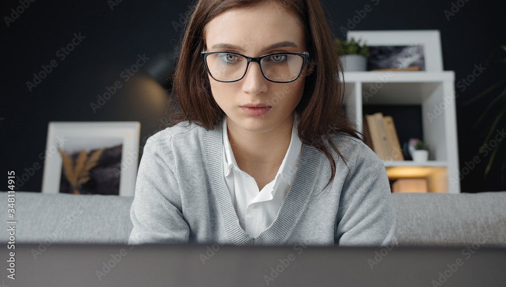 Headshot of young focused woman sitting on sofa working on laptop in flat, telemediated working Headshot of young focused woman sitting on sofa working on laptop in flat, telemediated working