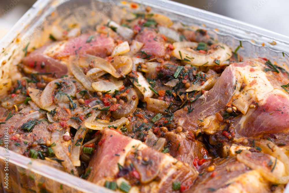 Raw marinaded juicy pork meat in plastic container. Fresh food prepared for barbeque. Summer cooking outdoors