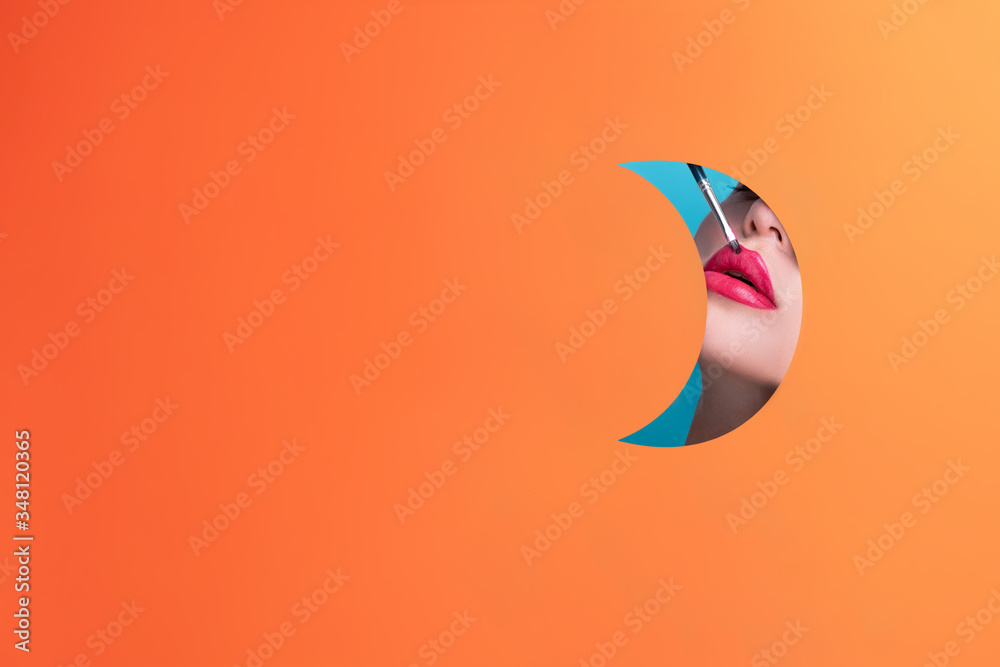 Φωτογραφία Big red lips of a model posing in a cut out figure in the form of an orange circle with a lip brush