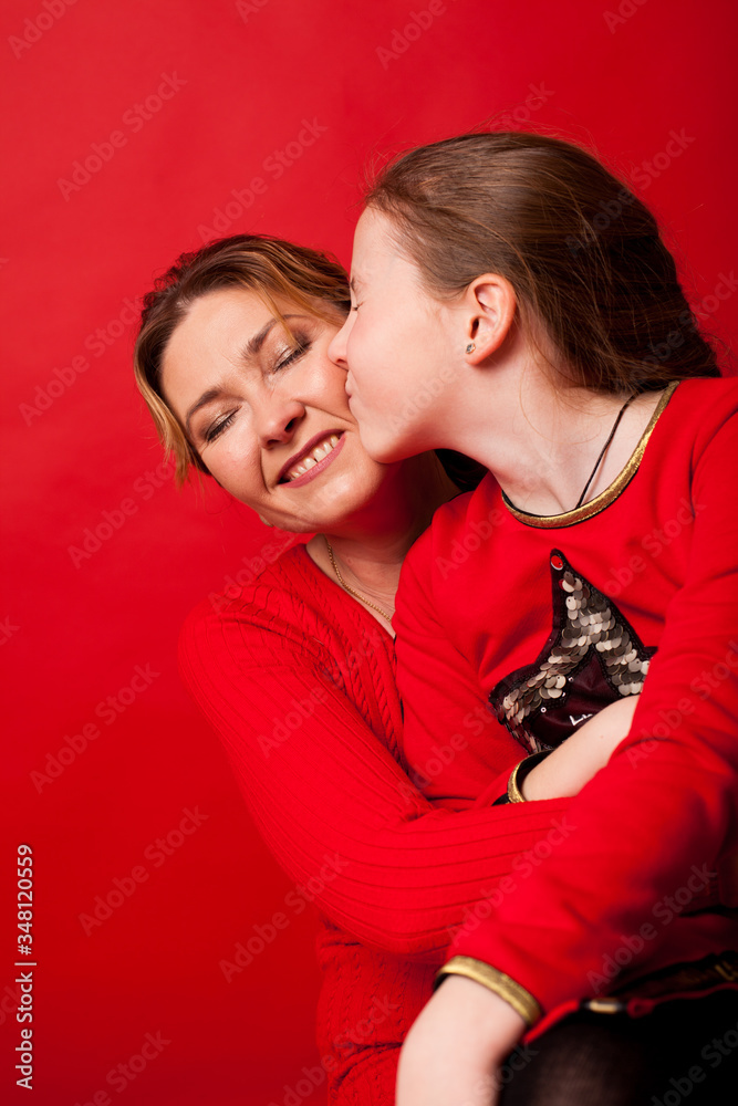 Mom and daughter lovingly cuddle on a red background Mom and daughter lovingly cuddle on a red background