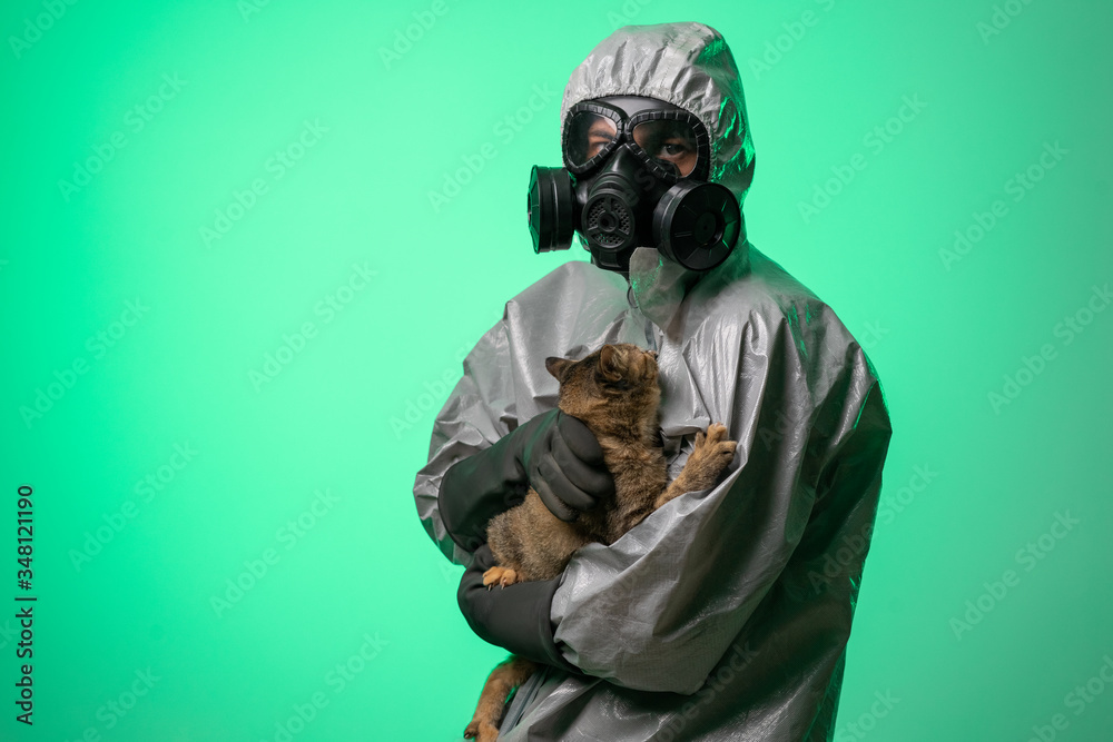 Scientist man in protective suit with scared cat in his hands is safe from coronavirus in medical protection mask. Pandemic world. Green background Scientist man in protective suit with scared cat in his hands is safe from coronavirus in medical protection mask. Pandemic world. Green background