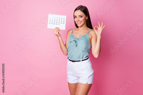 Portrait of her she nice-looking attractive lovely pretty charming content cheerful cheery girl showing ok-sign holding in hand paper calendar isolated over pink pastel color background