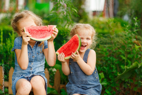 Little girls sit on watermelon and keep pieces 