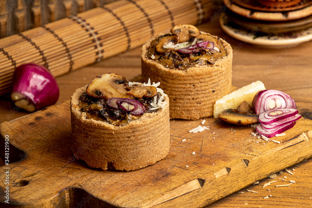 Tarts with mushrooms, caramelized red onion and cheese over on old wooden rustic background.