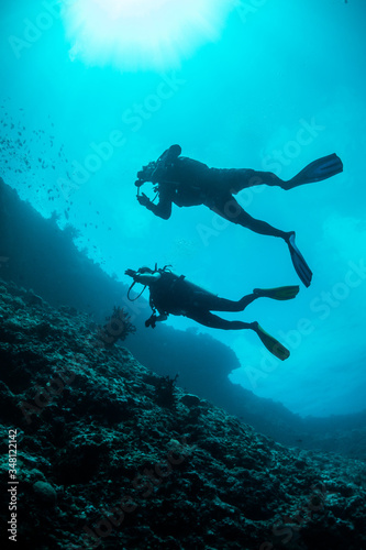 Silhouette of divers swimming in clear blue water around a coral reef