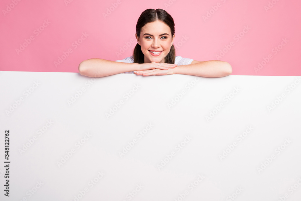 Photo of cheerful lady leaning hands on big empty paper poster proposing buy advertisement place wear casual white t-shirt isolated pastel pink color background Photo of cheerful lady leaning hands on big empty paper poster proposing buy advertisement place wear casual white t-shirt isolated pastel pink color background