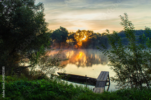 Morning. Sunrise on the river. There is a boat at the pier. Fog rises above the river.