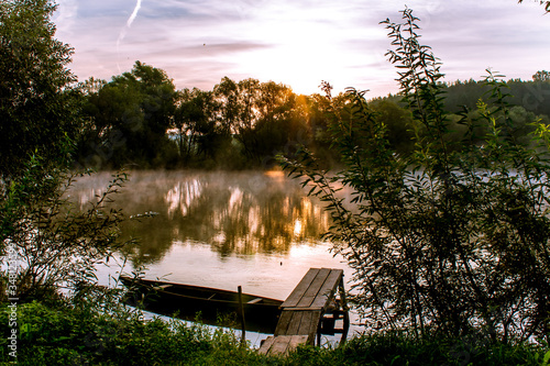 Ukraine. Early morning on the river. Sunrise.
Fog rises above the river. The rays of the sun make their way through
  foliage of coastal trees.