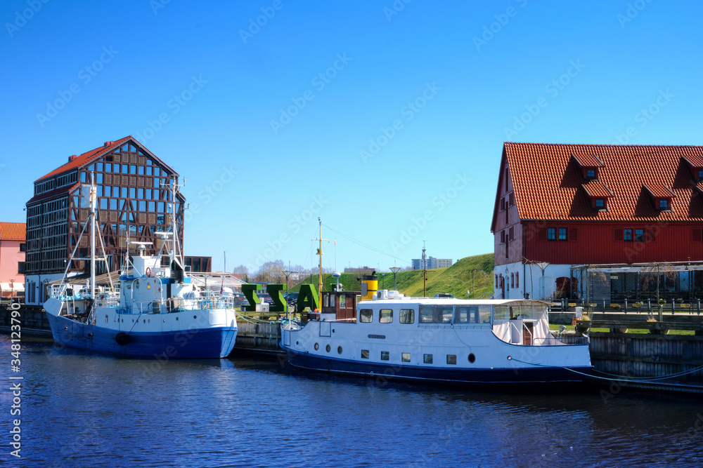 Jetty for boats and yachts in Klaipeda, Lithuania, on sunny day. Beautiful view of vessels and fachwerk and red-brick houses