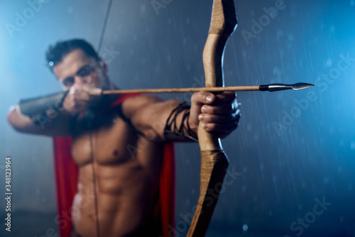 Muscular mature spartan shooting from bow.