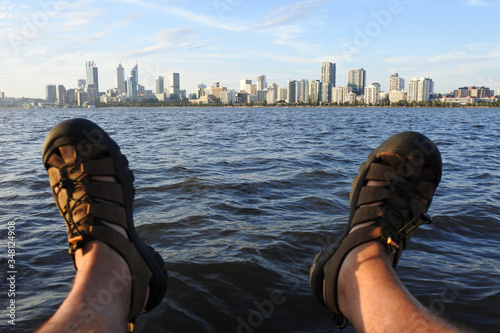 POV of person sitting on Swan River riverbank looking at the landscape view of Perth city financial centre skyline at sunset