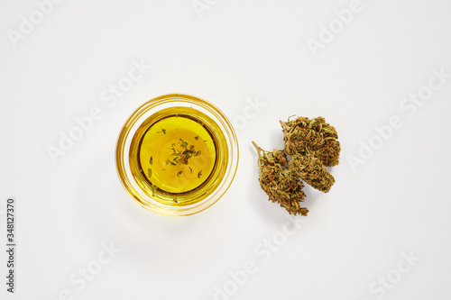 marijuana buds and a small bowl of cbd oil on a white background