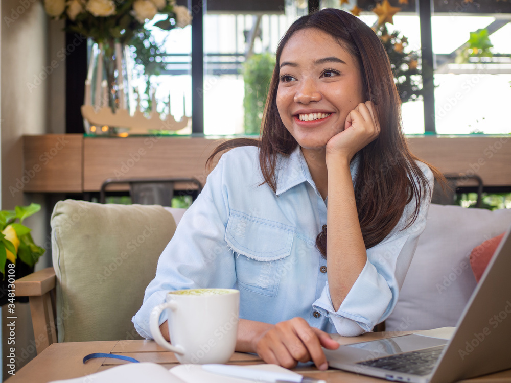 A beautiful Asian woman is sitting smiling and working comfortably on a laptop. In a coffee shop or restaurant A beautiful Asian woman is sitting smiling and working comfortably on a laptop. In a coffee shop or restaurant