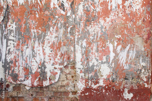 Old dirty wall with torn paper posters, peeling plaster and rough surface texture background.