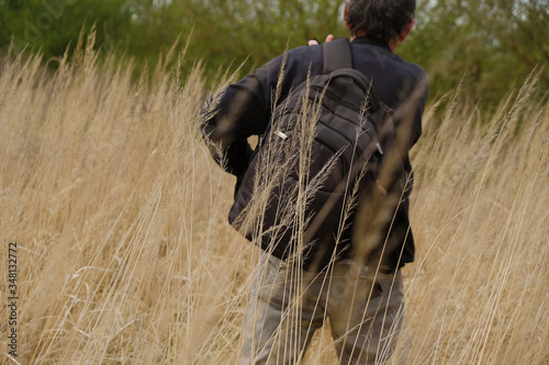 Silhouette of a man with his back with a black backpack among the dry tall grass. Tourism in the wild in Ukraine. Copy space.