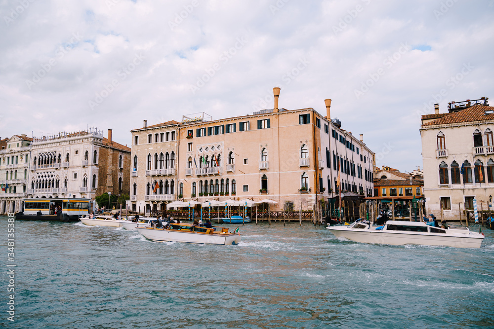 Tourists on the waterfront in Venice, against the background of the ancient facades of buildings standing in the water. Water sightseeing in Venice, Italy.