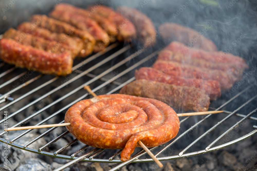 Sausages and traditional romanian sausages called ”mici” or ”mititei” (dish consisting of grilled ground meat rolls in cylindrical shape made from a mixture of meat and spices) on barbecue with smoke