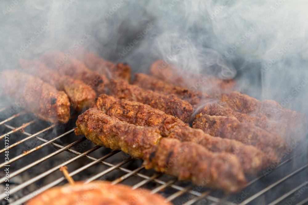 Sausages and traditional romanian sausages called ”mici” or ”mititei” (dish consisting of grilled ground meat rolls in cylindrical shape made from a mixture of meat and spices) on barbecue with smoke Sausages and traditional romanian sausages called ”mici” or ”mititei” (dish consisting of grilled ground meat rolls in cylindrical shape made from a mixture of meat and spices) on barbecue with smoke