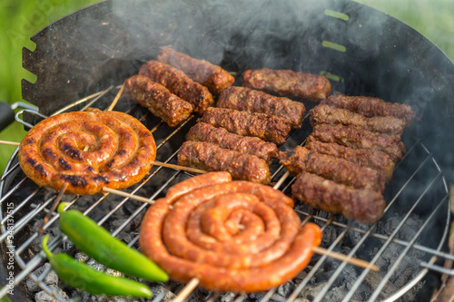 Sausages and traditional romanian sausages called ”mici” or ”mititei” (dish consisting of grilled ground meat rolls in cylindrical shape made from a mixture of meat and spices) on barbecue with smoke