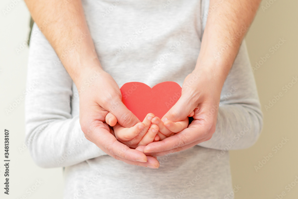 Paper red heart in hands of male dad and little child girl on yellow background at home. Concept of a healthy family. Paper red heart in hands of male dad and little child girl on yellow background at home. Concept of a healthy family.