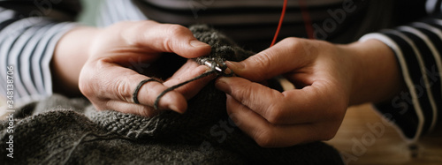 Close up photo of woman's hands knitting on grey yarn on wooden