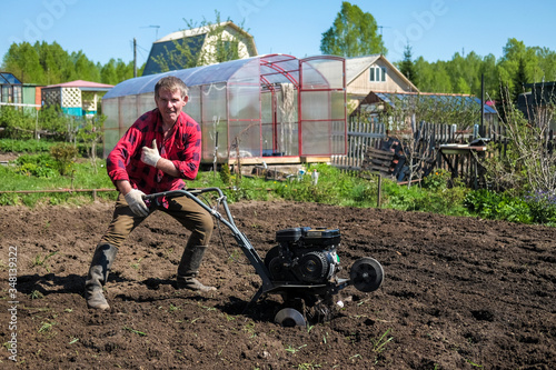 Old man plows the ground with a motor cultivator. A farmer ploughs the soil using a petrol cultivator.