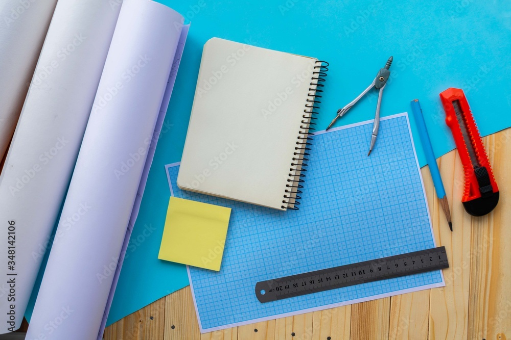 Still life, business, stationery or education concept: top image with blank pages, notebook, ruler, pencil, clerical knife, compass on a wooden and blue background, ready to be added or mock up Still life, business, stationery or education concept: top image with blank pages, notebook, ruler, pencil, clerical knife, compass on a wooden and blue background, ready to be added or mock up
