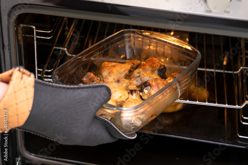 Fotografie hand in a refractory glove takes out a dish with baked chicken legs from the ove
